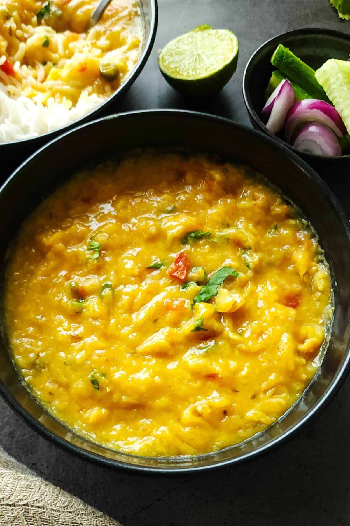 Masoor dal served in a black bowl with salad and half a slice of lime in the background.