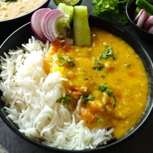 Moong Masoor dal, rice, and salad, served in a black bowl.