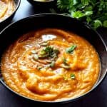 Moroccan sweet potato and chickpea soup garnished with pumpkin seeds and herbs served in a bowl.