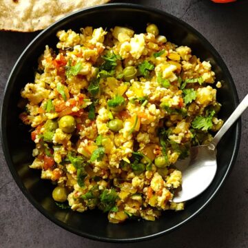 Paneer bhurji in a black bowl with a spoon.
