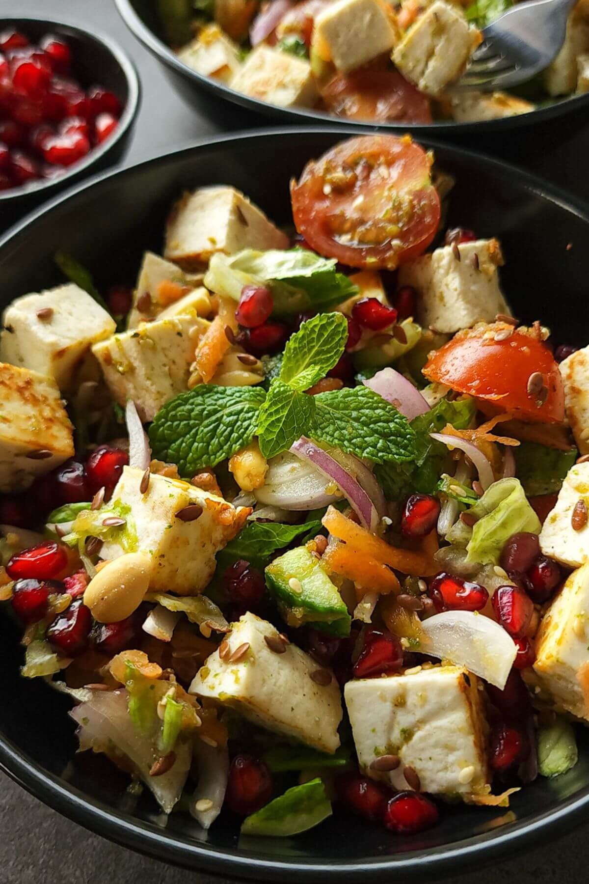 Indian salad with paneer served in a black bowl.