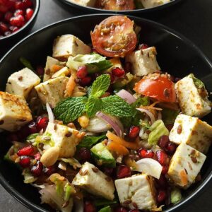Paneer salad garnished with mint leaves served in a black bowl.