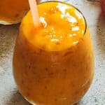 Peach mango smoothie in a glass with a straw.