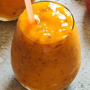 Peach mango smoothie in a glass with a straw.