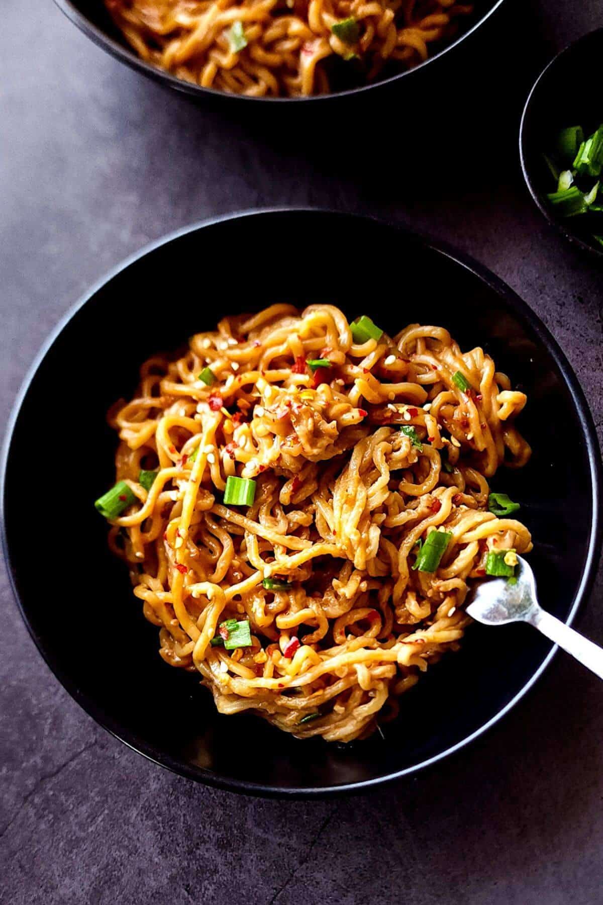 Spicy peanut noodles served in a black bowl with a fork.