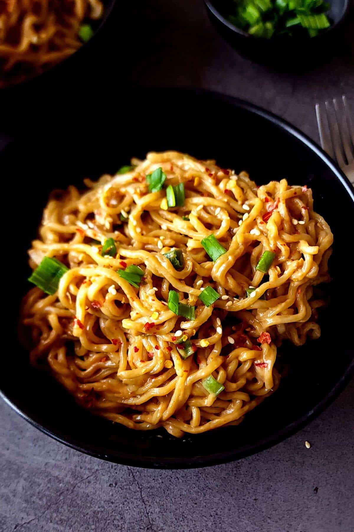 Peanut sauce noodles in a black bowl with a fork on the side.