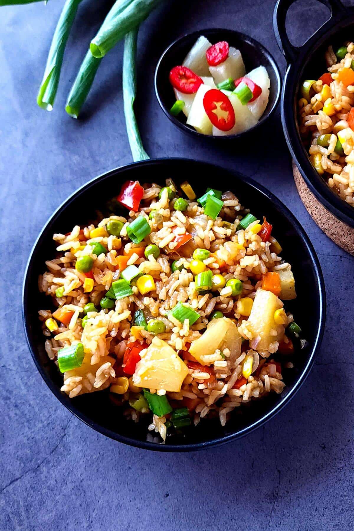 Pineapple fried rice with vegetables served in a black bowl.