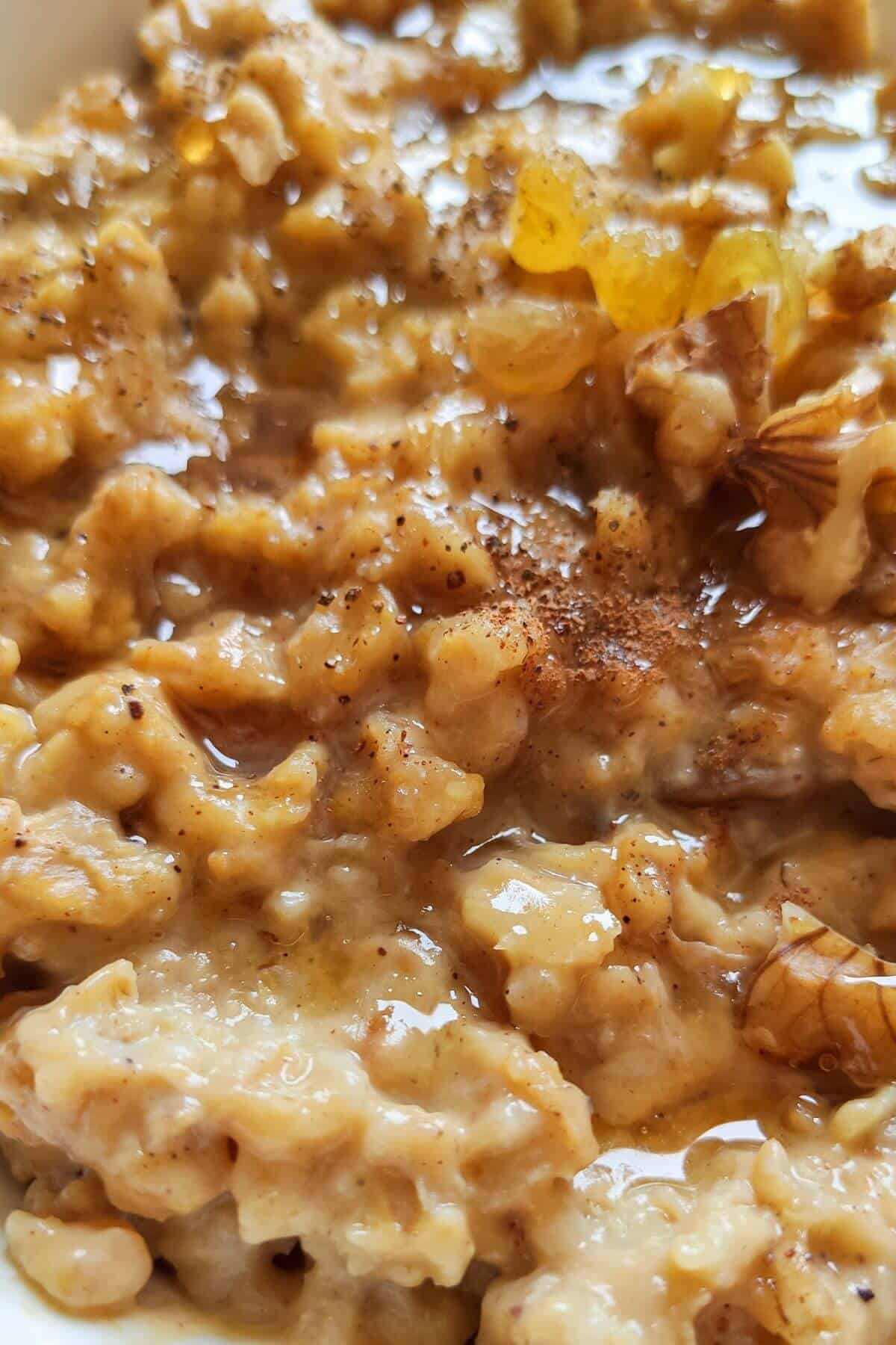 Close up shot of pumpkin oatmeal topped with walnut kernel, maple syrup, and cinnamon powder
