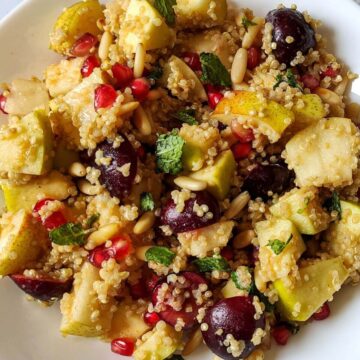 Quinoa fruit salad garnished with fresh mint leaves served on a white plate.