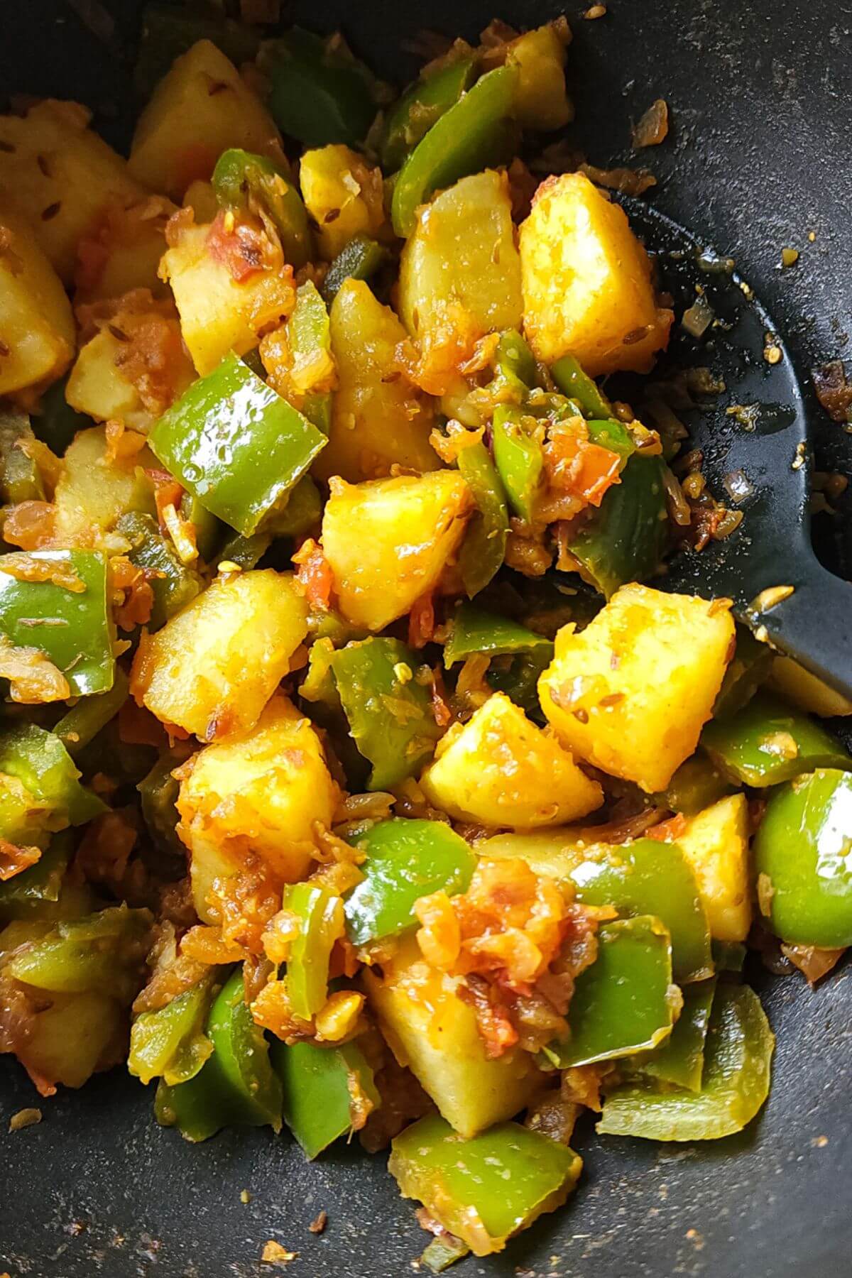 Indian style capsicum and potatoes in a pan with a spatula.