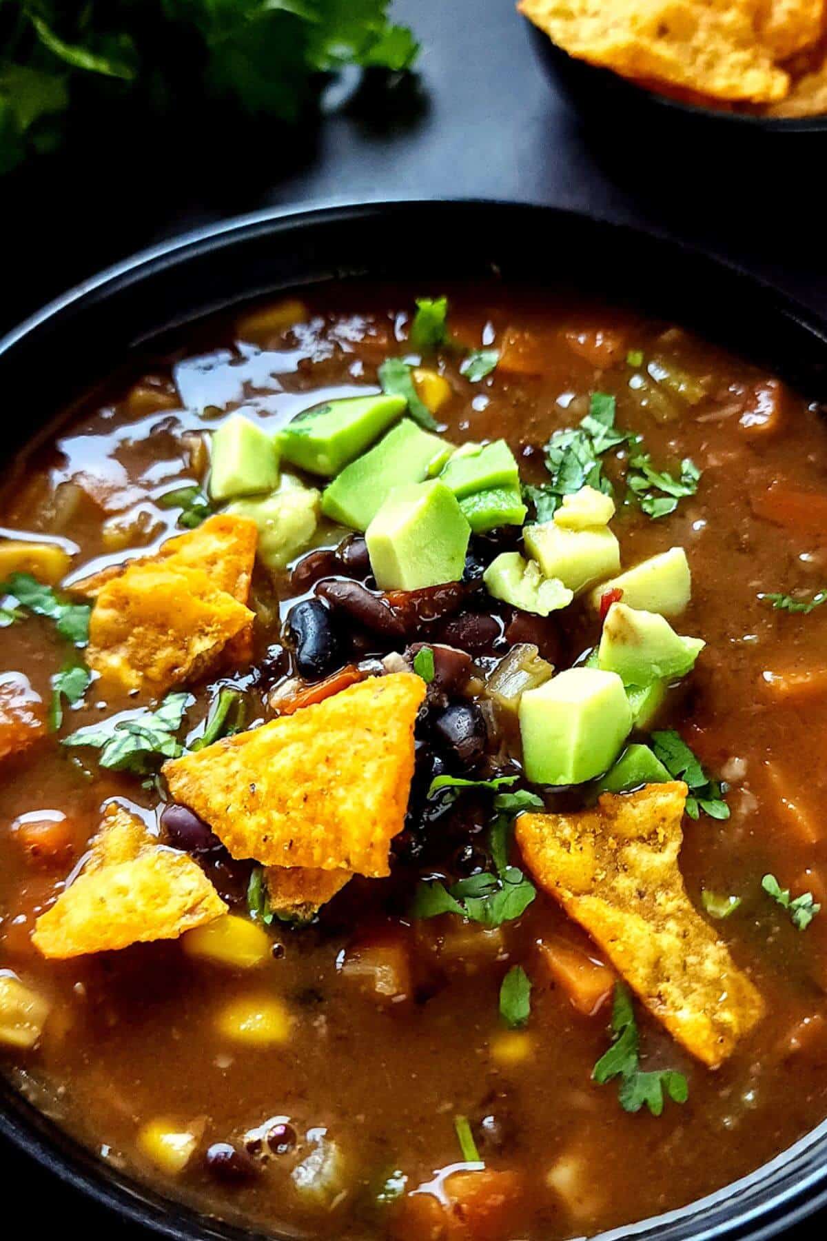 Vegetarian black bean soup topped with chopped avocado and tortilla chips in a bowl.