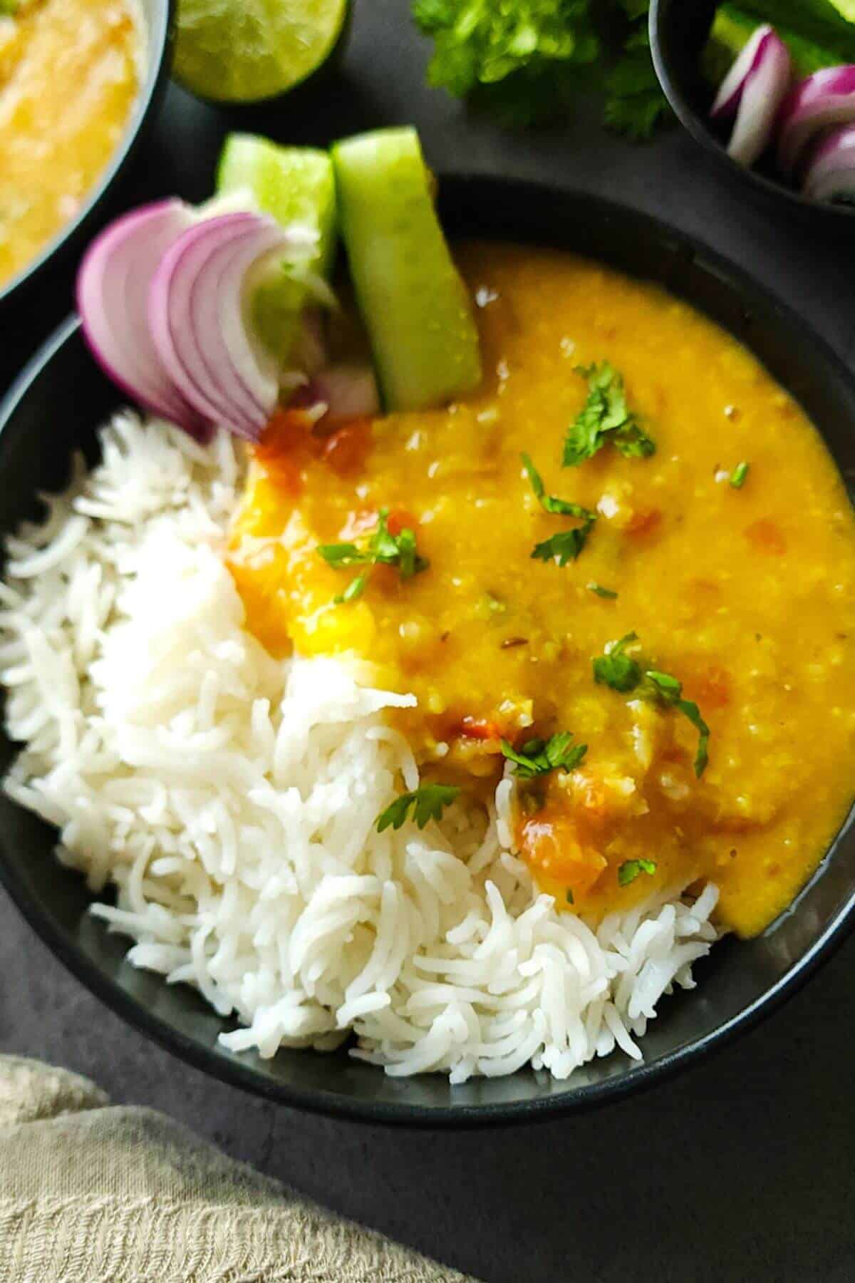 Moong Masoor dal served with rice and salad in a black bowl.