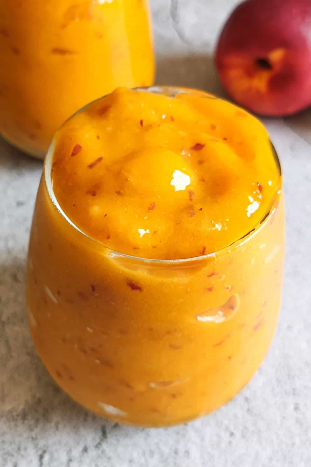 Two glasses of Peach mango smoothie with a peach in the background