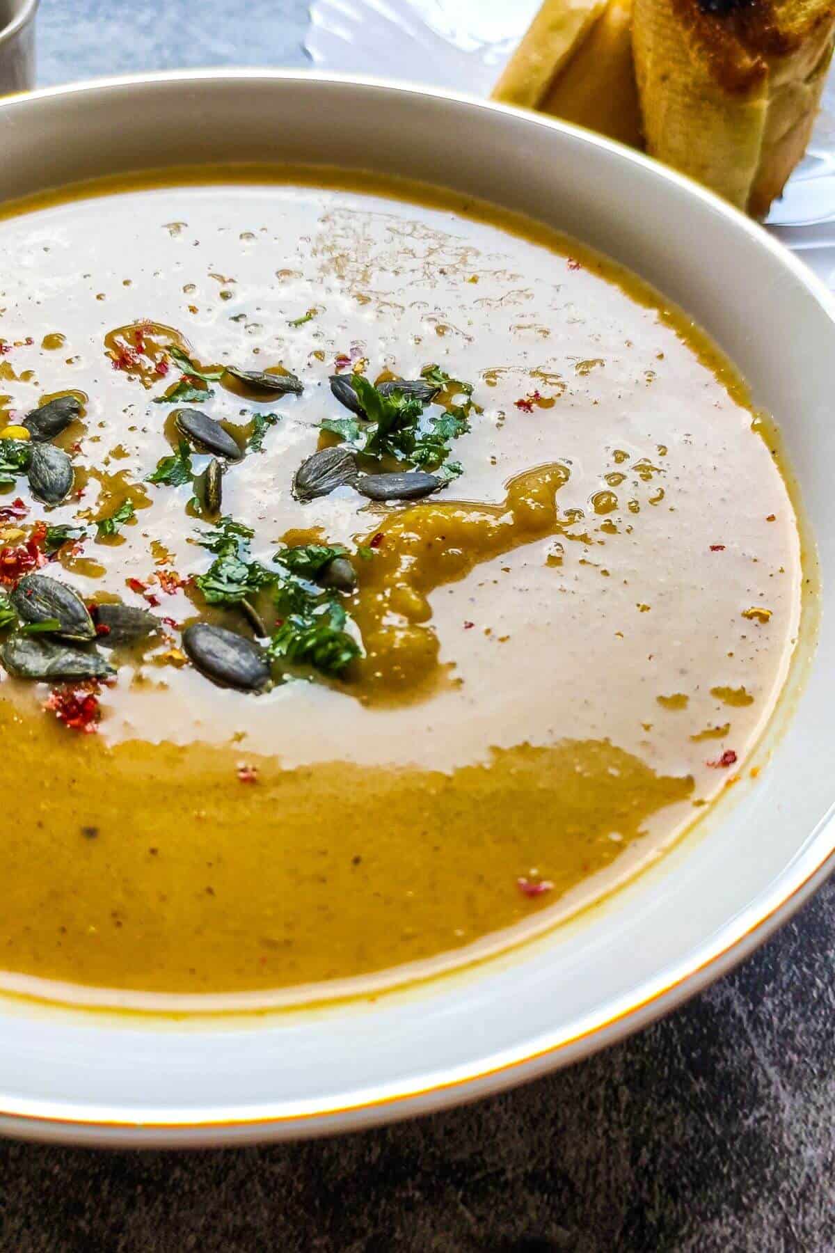 A bowl of vegan pumpkin soup garnished with herbs, pepitas, and chili flakes.