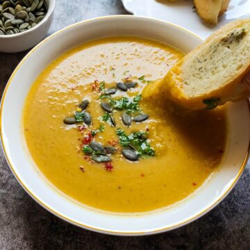 Roasted pumpkin soup in a bowl with a bread slice.
