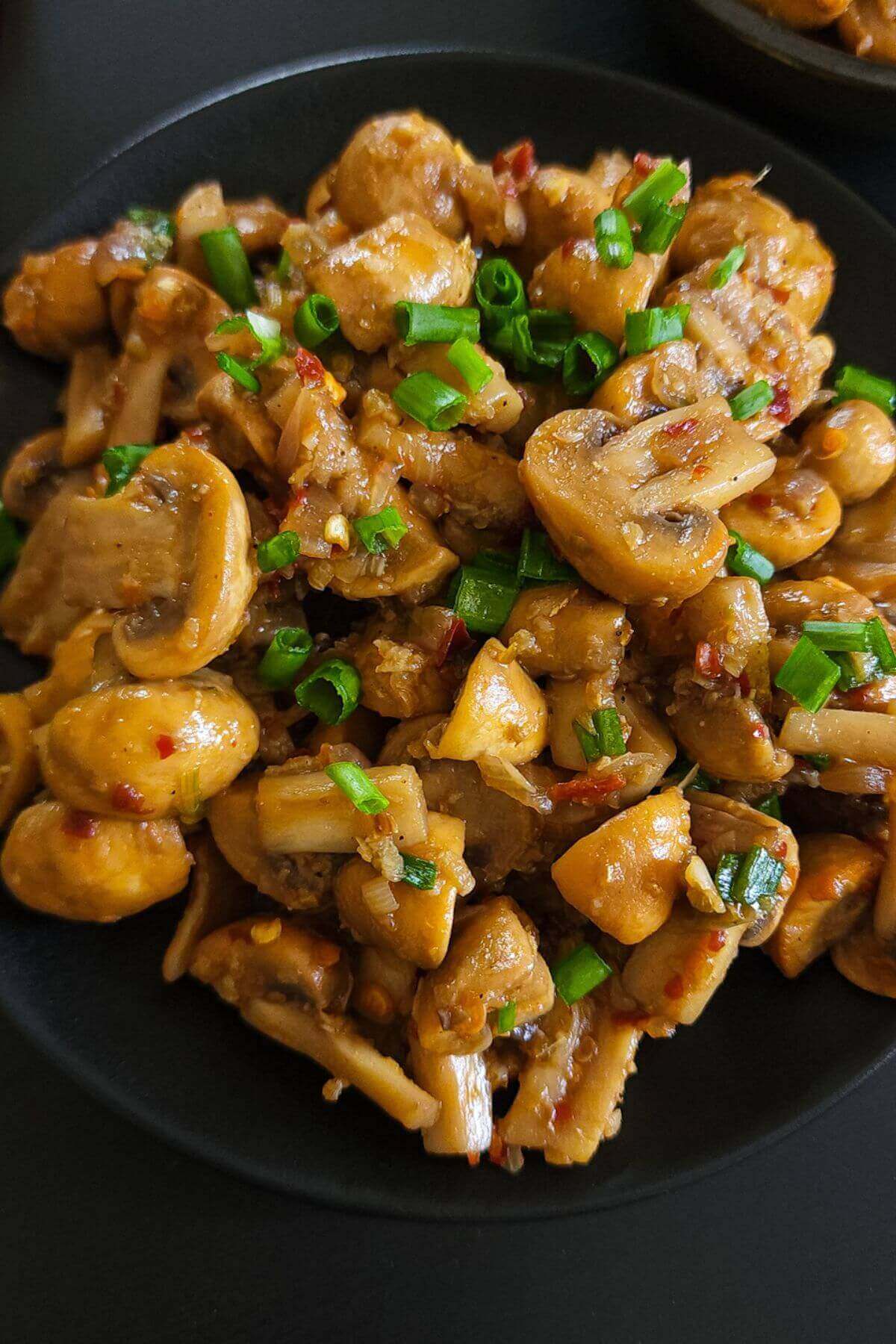 Spicy garlic mushrooms served on a black plate.
