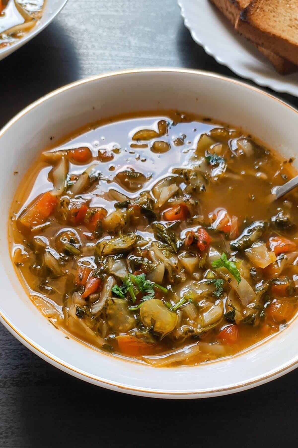 Vegetarian cabbage soup served in a white bowl with toasted bread in the background.