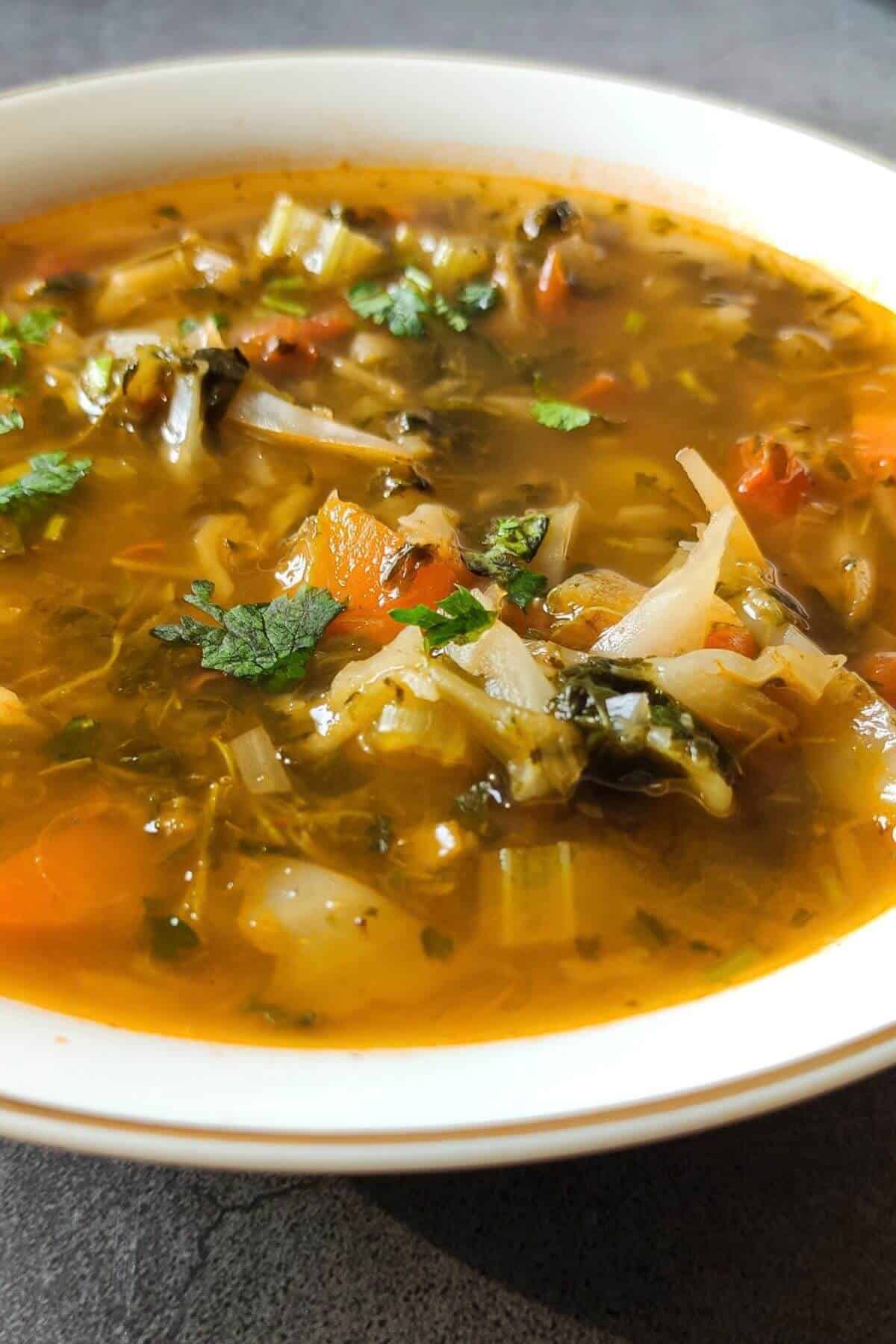 Cabbage soup with vegetables in a white bowl.