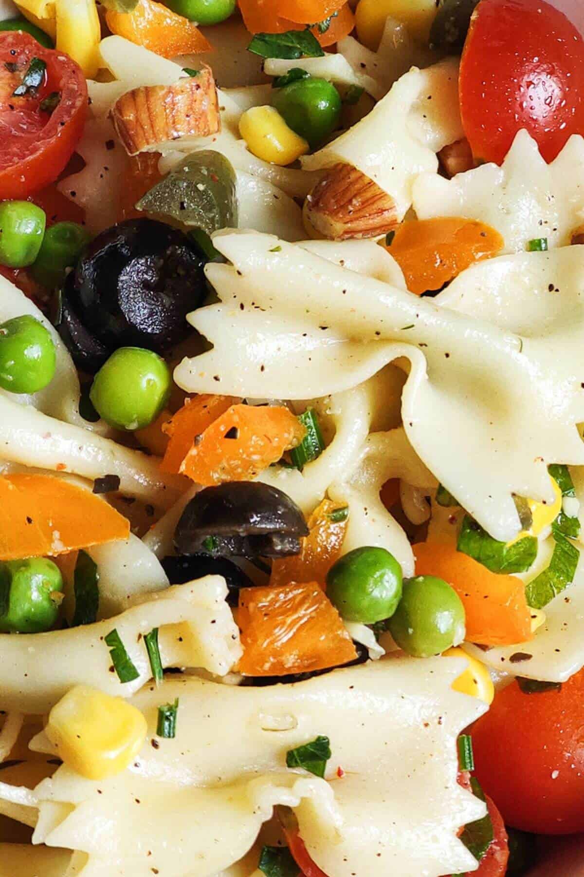 Close up shot of vegan pasta salad with green peas, olives, cherry tomatoes, and sweet corn.
