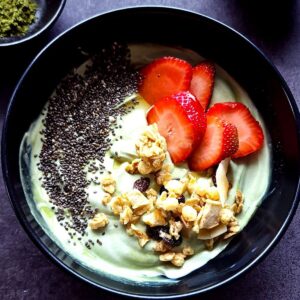 A bowl of matcha yogurt with granola, chia seeds, and sliced strawberries.