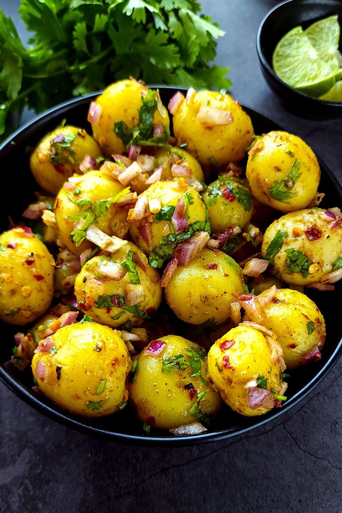 Indian baby potato salad served in a black bowl with cilantro and lime wedges in the background.
