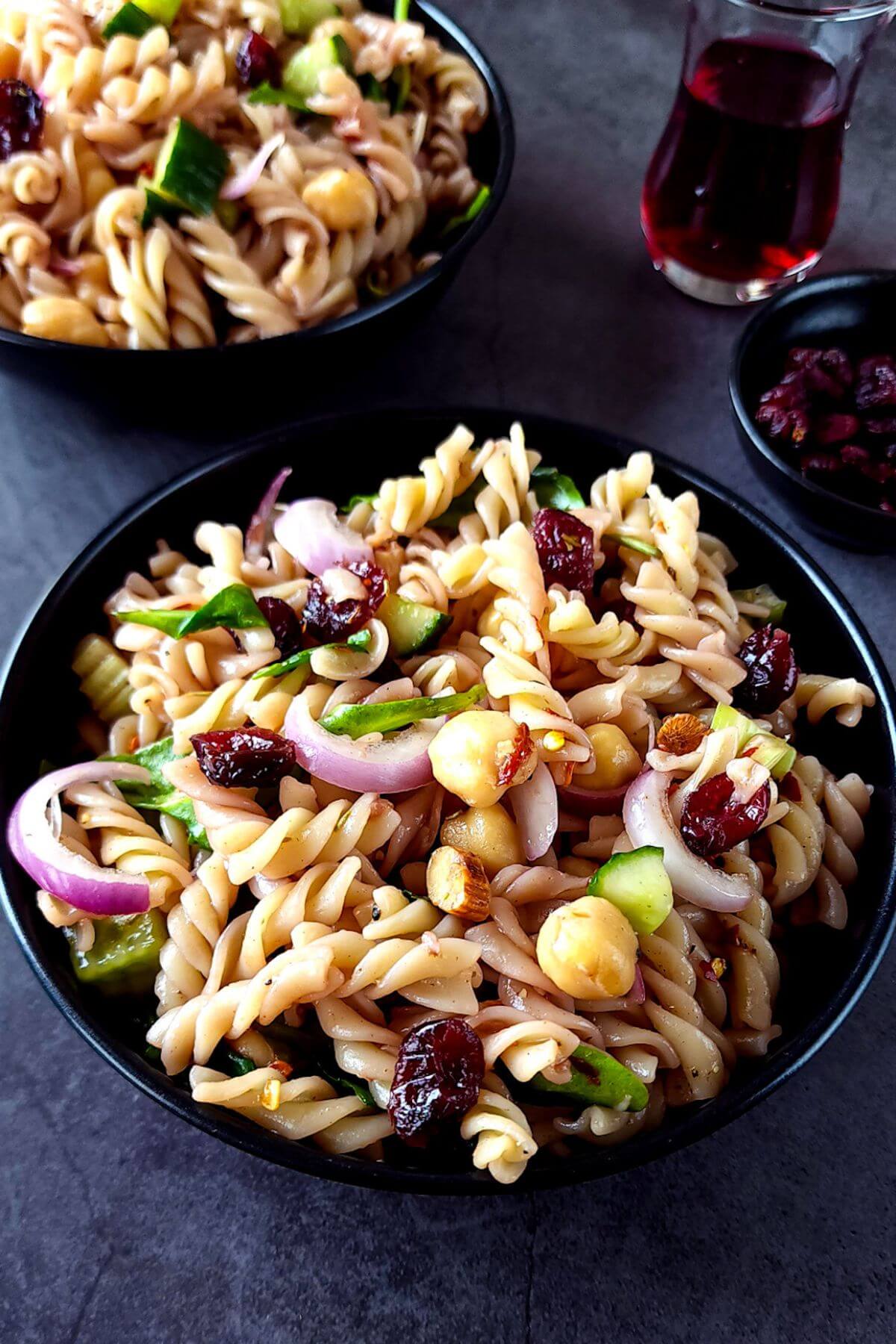 Two bowls of cranberry pasta salad with a glass of cranberry juice in the background.