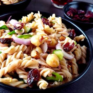 A bowl of cranberry pasta salad with a bowl of dried cranberries in the background.
