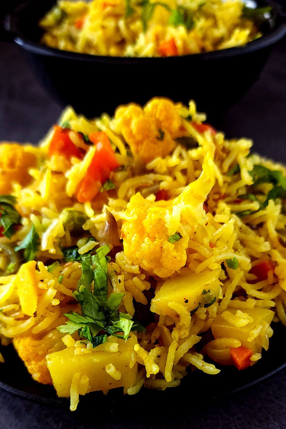 Spiced basmati rice with vegetables served on a black plate.
