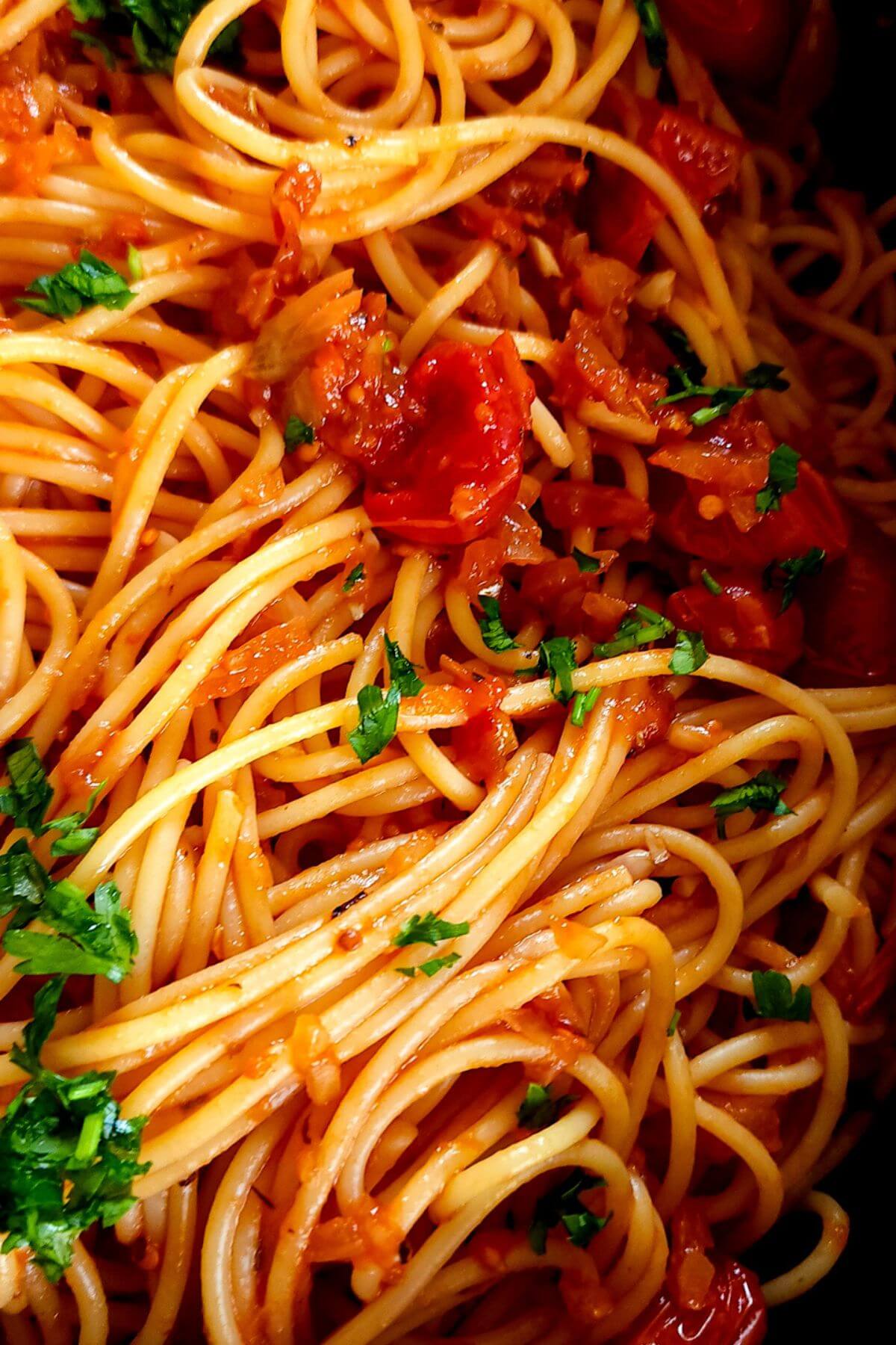 Close up shot of spaghetti napolitana garnished with chopped parsley.