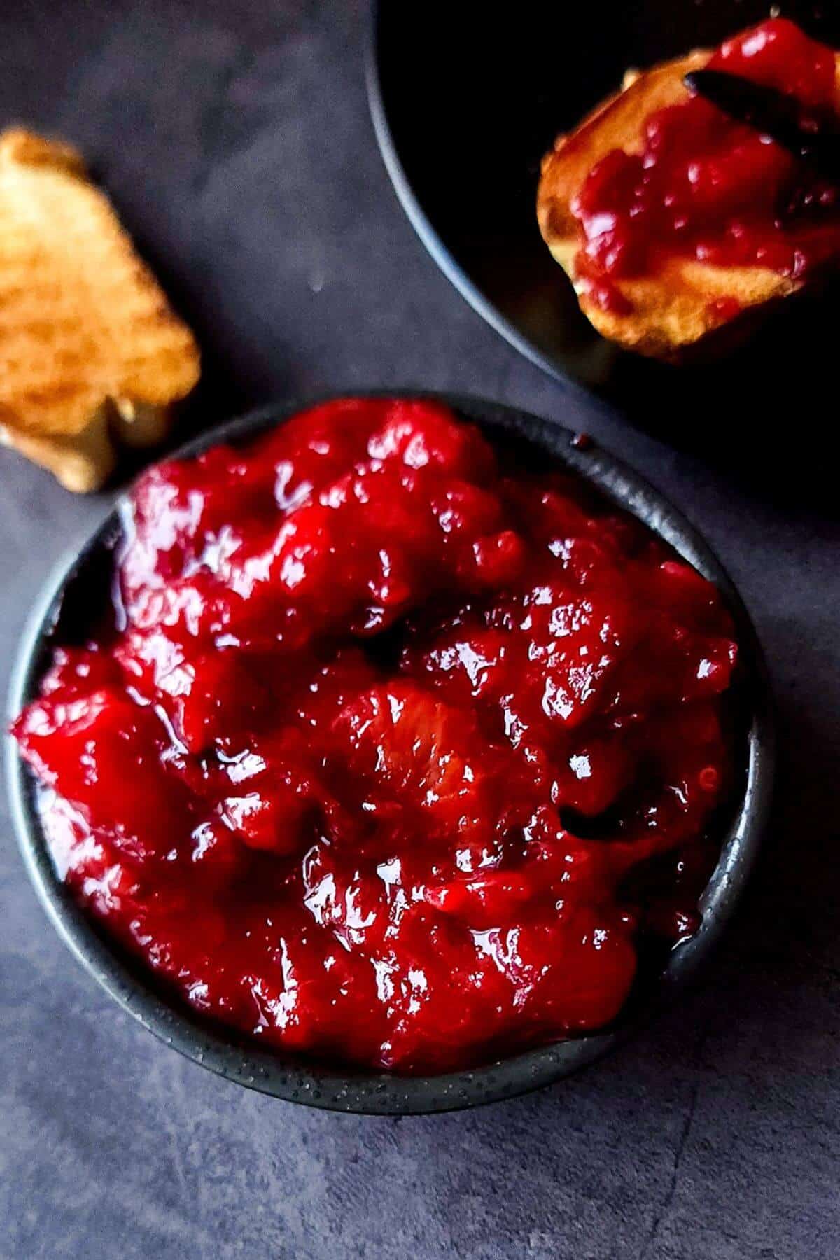 Plum chutney in a black bowl with toasted bread in the background.