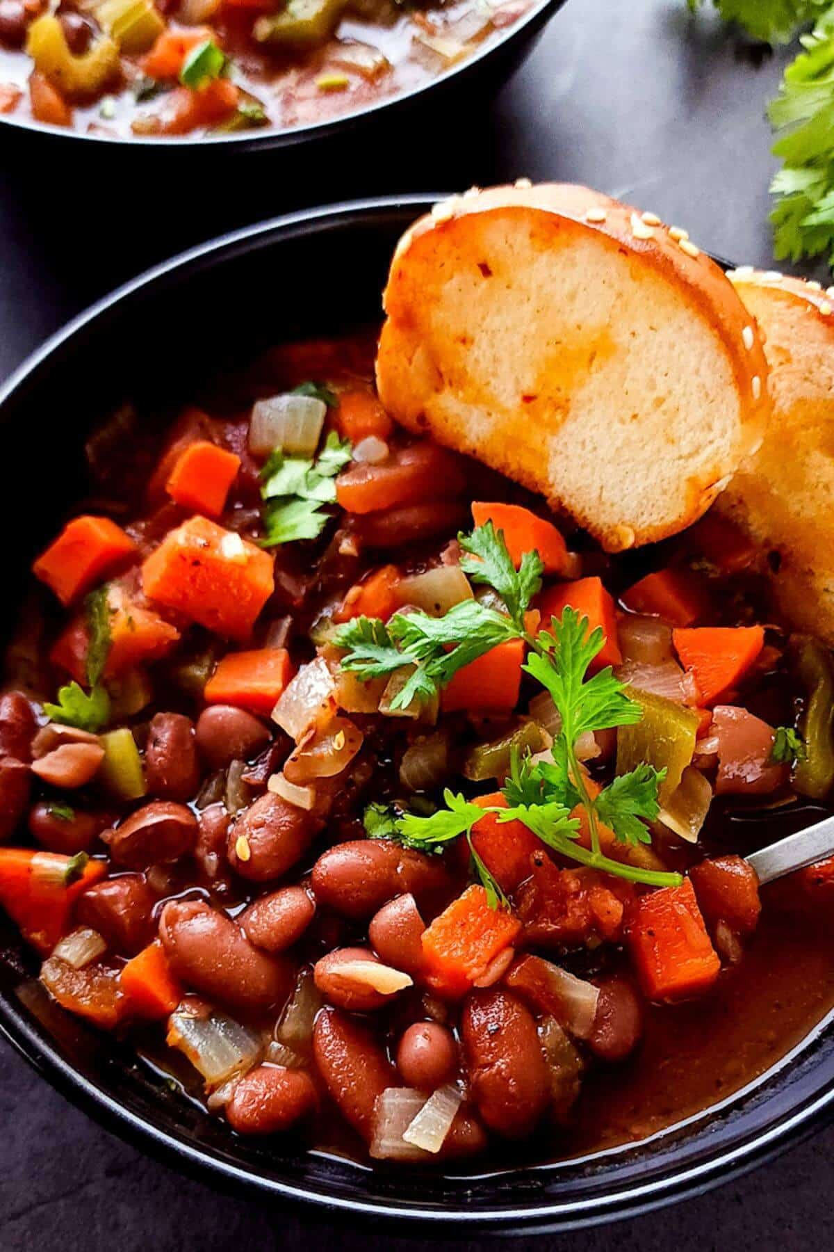Kidney bean stew in a black bowl with toasted bread slices.