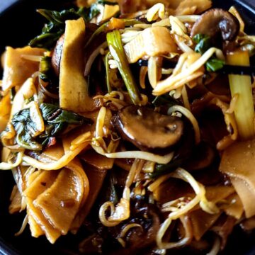 Close up shot of ho fun noodles with mushrooms and bean sprouts.