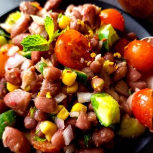 Rajma salad with cherry tomatoes, sweet corn, and cucumber on a black plate.