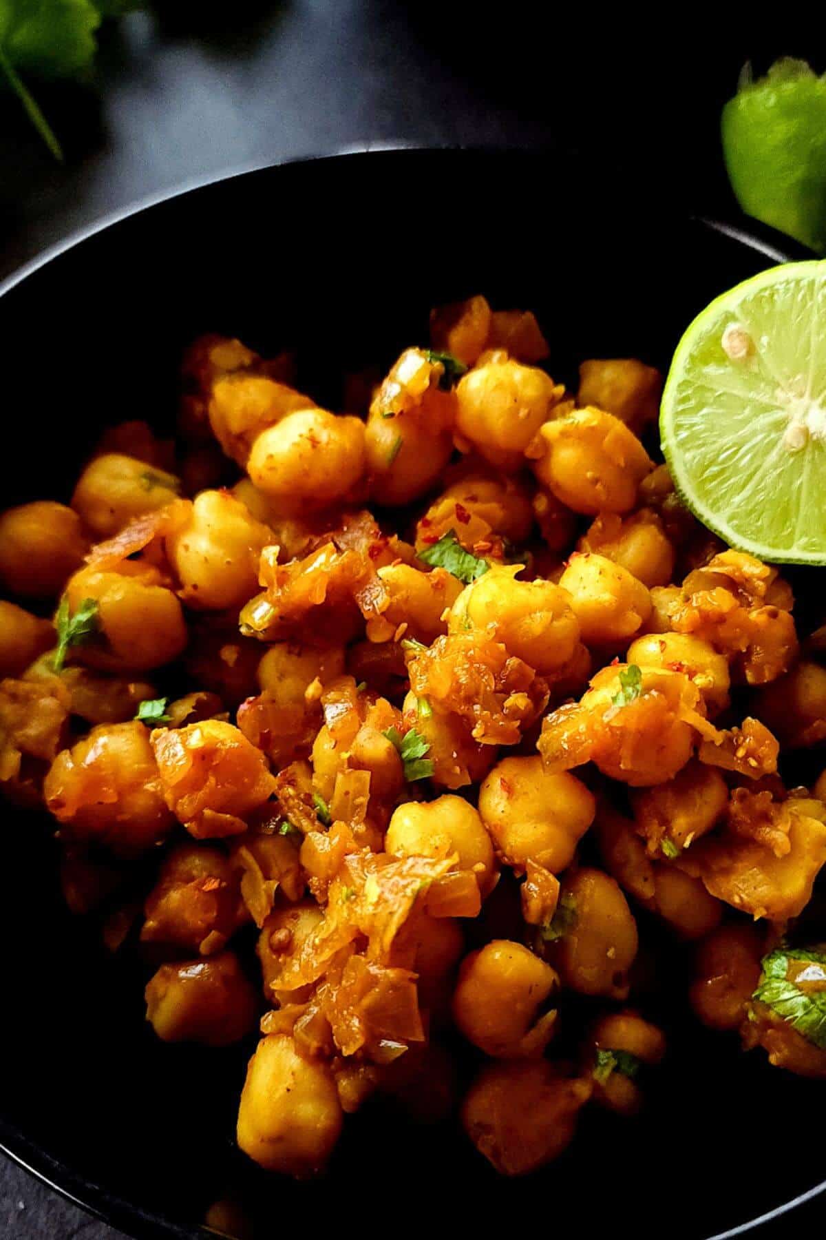 Sauteed chickpeas served in a black bowl with a slice of lime.