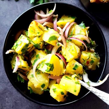 A bowl of Armenian potato salad with onion and fresh herbs.