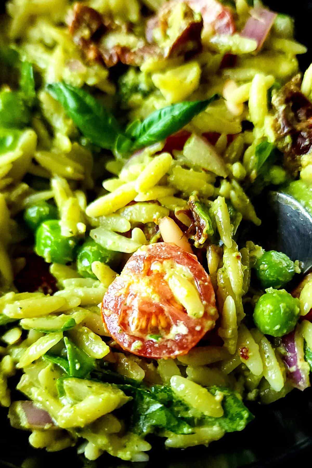Orzo salad with pesto, cherry tomatoes, and green peas in a bowl.
