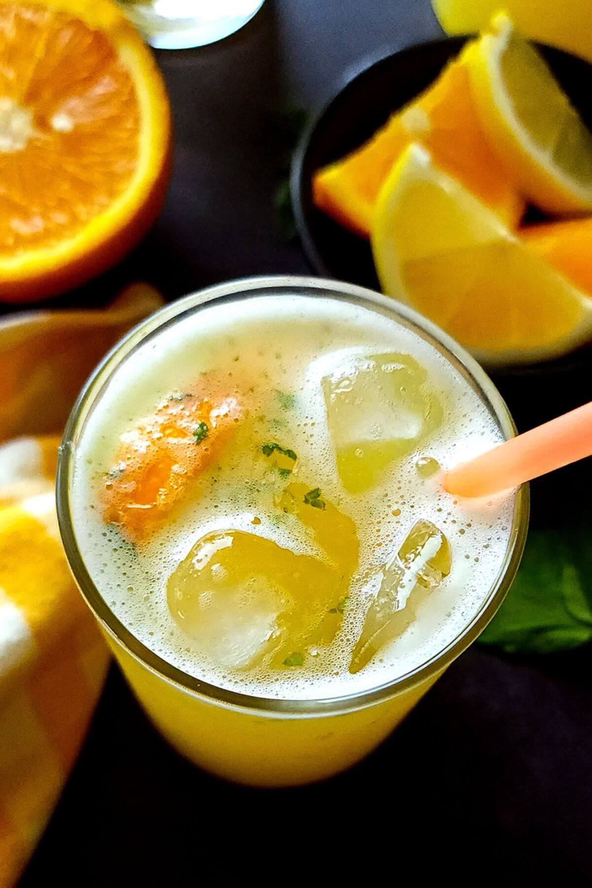 A glass of homemade orange lemonade with orange wedges in the background.