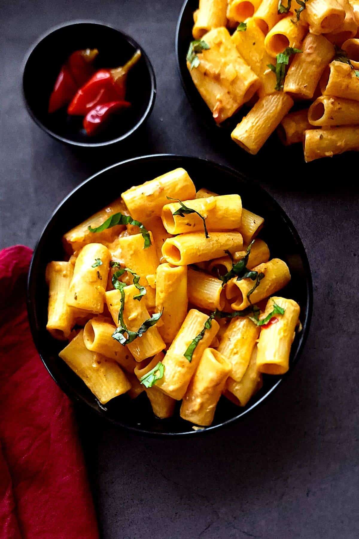 Two bowls of spicy rigatoni with a small bowl of calabrian chili peppers.