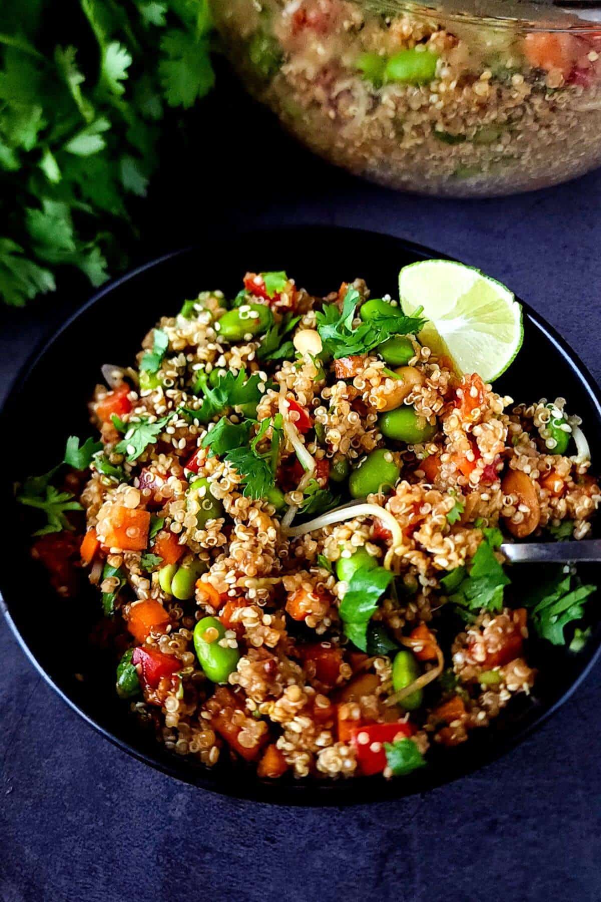 Vegan Asian quinoa salad with edamame in a black bowl.