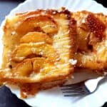 Two peach upside down puff pastries served on a plate with a fork.