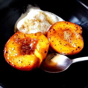 Pan fried peaches with ice cream and a spoon served on a black plate.