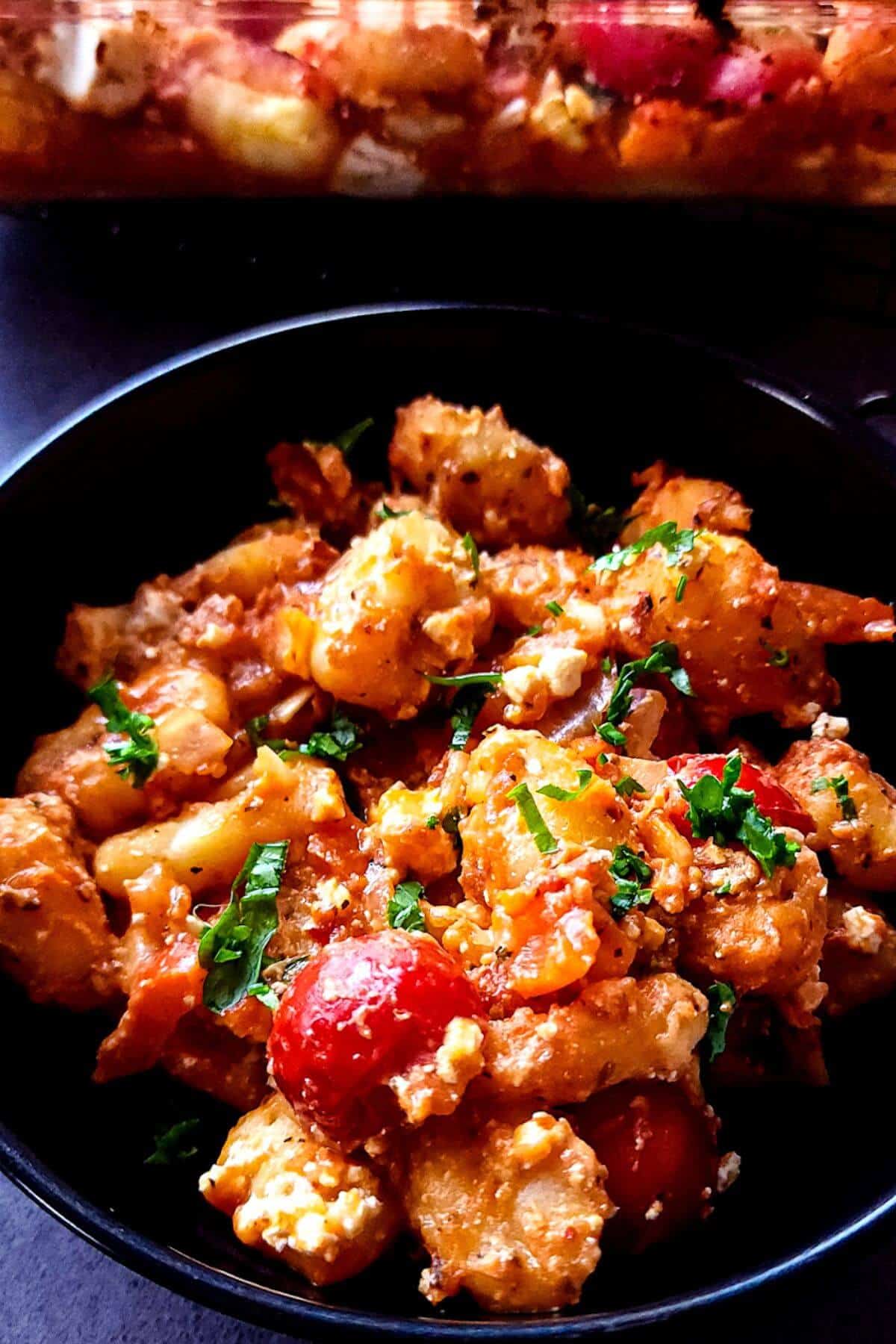 Baked gnocchi with feta and tomatoes in a black bowl.