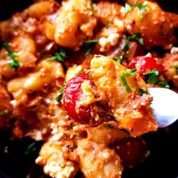 A spoonful of vegetarian baked gnocchi lifted over a bowl of baked tomato gnocchi.