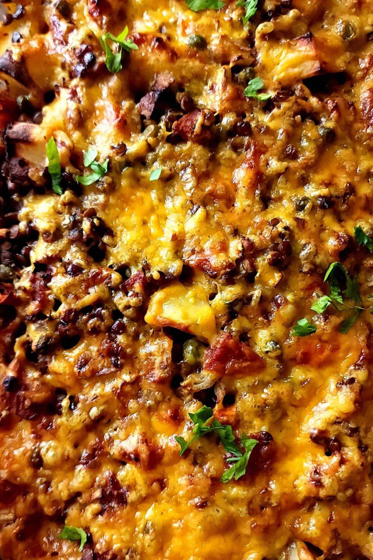 Baked lentil casserole with cheese and vegetables garnished with chopped parsley.