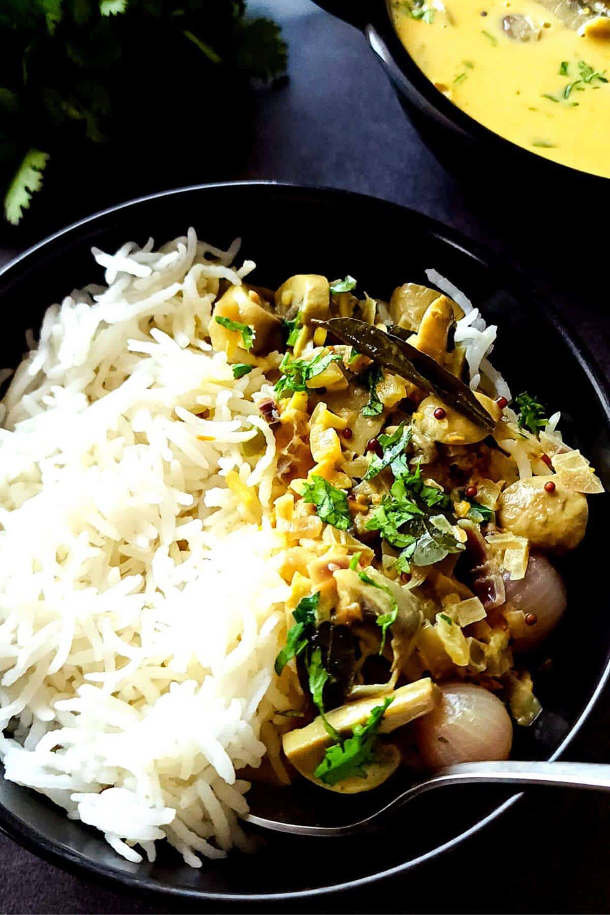 Rice and mushroom coconut curry in a black bowl with a spoon.