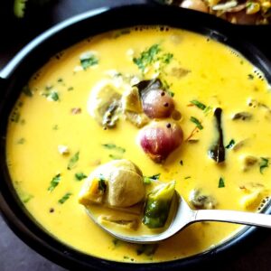 Mushroom curry with coconut milk in a black bowl with a spoon.