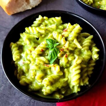Two bowls of creamy zucchini pasta with a baguette on the side.