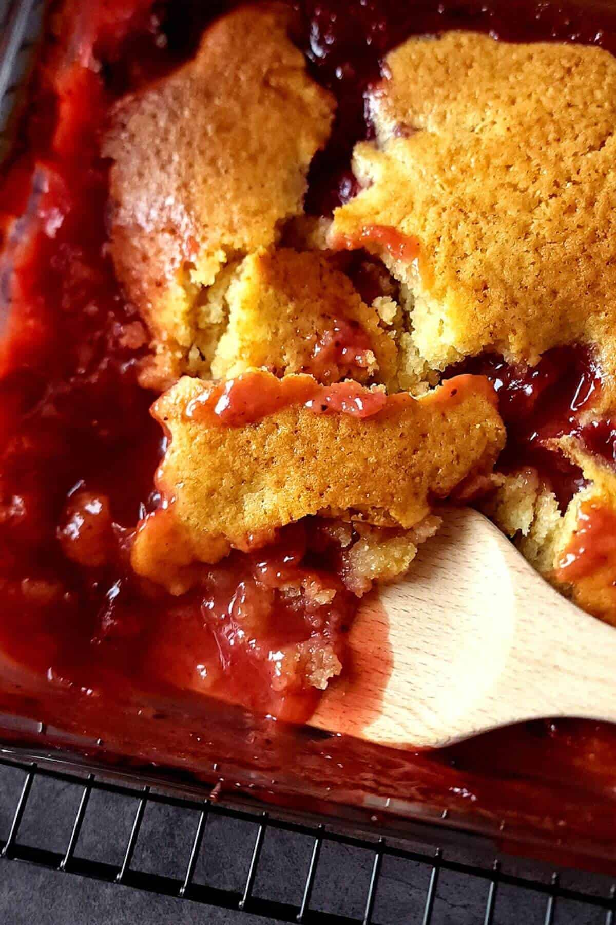 Fresh plum cobbler in a baking dish with a spatula.
