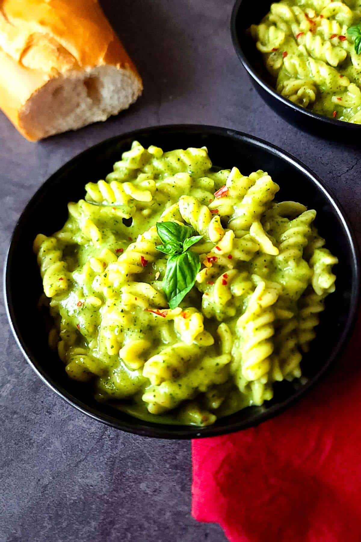Two bowls of creamy zucchini pasta with a baguette on the side.