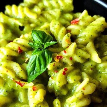 Pasta in zucchini sauce garnished with basil leaves and red pepper flakes.